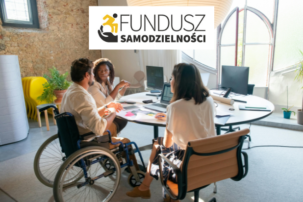 Dwie kobiety i jeden mężczyzna siedzą przy biurku. Mężczyzna siedzi na wózku